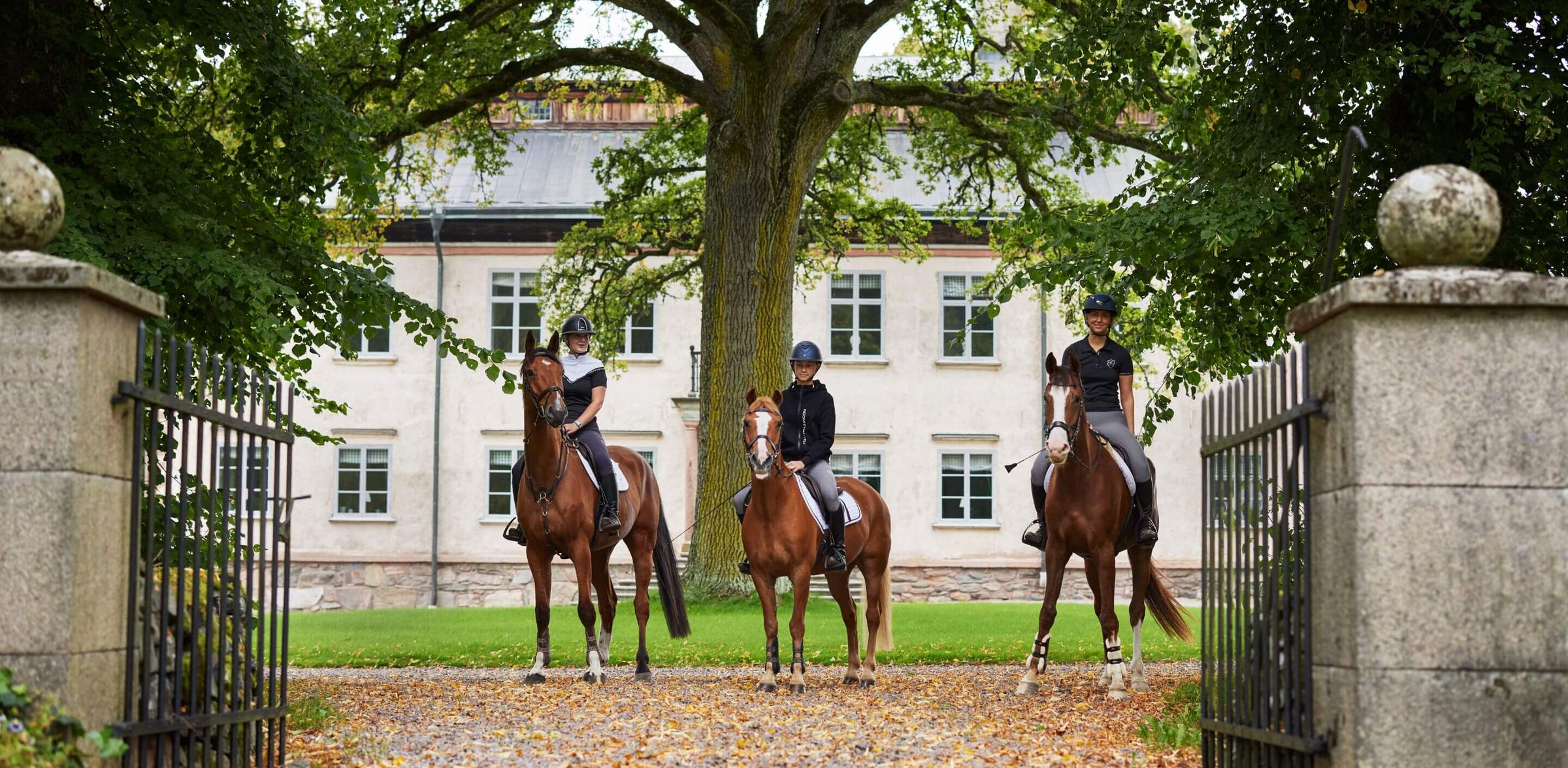 Inspirationsbild av tre stycken ryttare på var sin häst framför en herrgård. Ryttarna har på sig Noomi Chantell ridkläder 