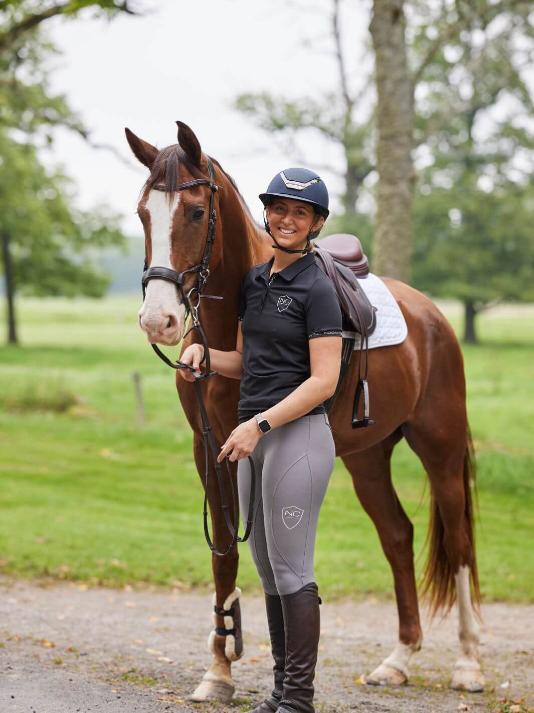 Model in Noomi Chantell riding attire standing next to a horse with an autumnal background